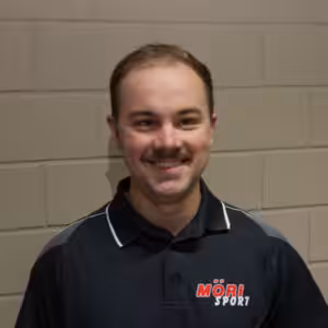 Ein lächelnder Mann in einem Mörsport-Poloshirt steht vor einer beigen Wand.