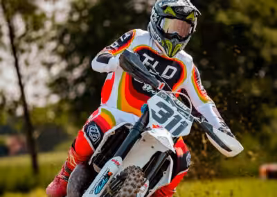 Motocross-Fahrer in Aktion bei Schwadernaurennen, bunte Ausrüstung, dynamische Kurve, staubige Rennstrecke.