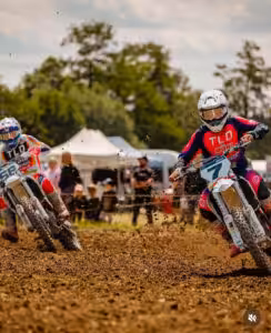 Motocross-Rennen im Freien: Zwei Fahrer in Action auf einer schlammigen Strecke mit Bäumen im Hintergrund.