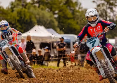 Motocross-Rennen im Freien: Zwei Fahrer in Action auf einer schlammigen Strecke mit Bäumen im Hintergrund.