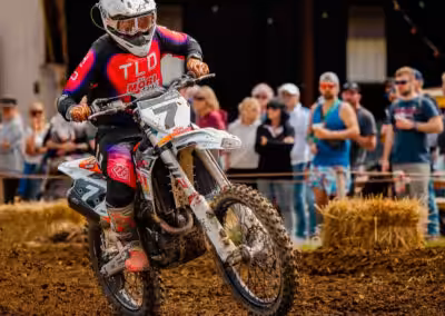 Motocross-Fahrer bei einem Rennen auf schlammiger Strecke, beobachtet von einer begeisterten Menschenmenge.