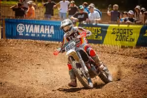 Motocross-Fahrer in TLD-Rennanzug beschleunigt auf schlammiger Strecke bei Yamaha-Event, Zuschauer im Hintergrund.