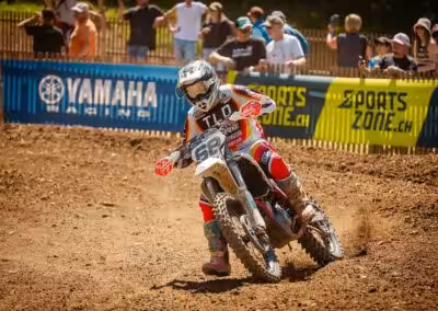 Motocross-Fahrer in TLD-Rennanzug beschleunigt auf schlammiger Strecke bei Yamaha-Event, Zuschauer im Hintergrund.